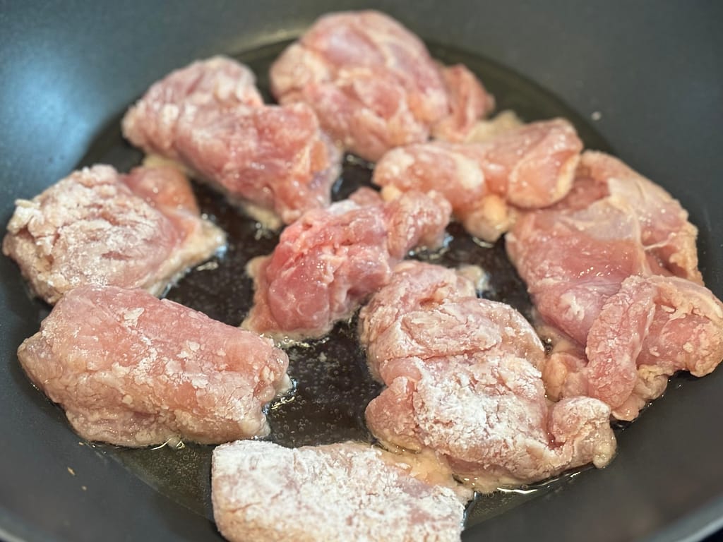 片栗粉をまぶした鶏肉をフライパンで焼いているところ。表面にうっすら焼き色がつき始めている。