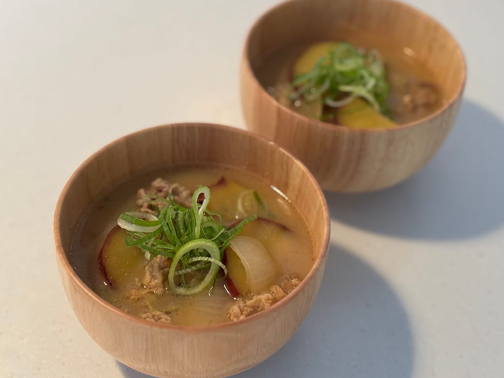 バーミキュラ ユキヒラで作った豚肉とさつまいもの味噌汁を木製の器に盛り付けた和食レシピ。仕上げにネギをトッピング