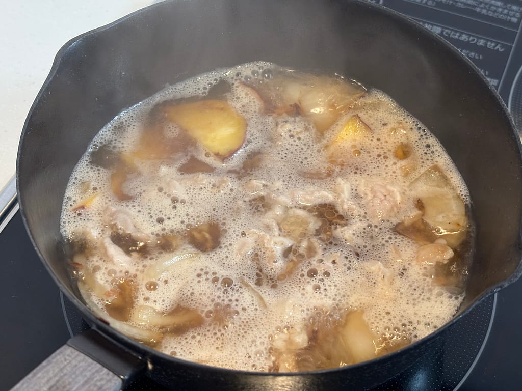 煮立っただし汁の中で豚肉と野菜を煮込んでいる途中の場面