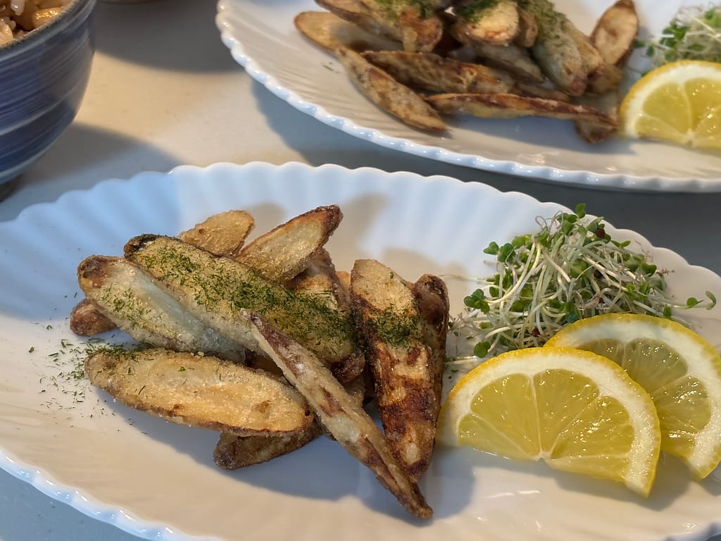 ごぼうの唐揚げとスプラウト、レモンを盛り付けた白い皿。食卓の副菜としての和風メニュー。