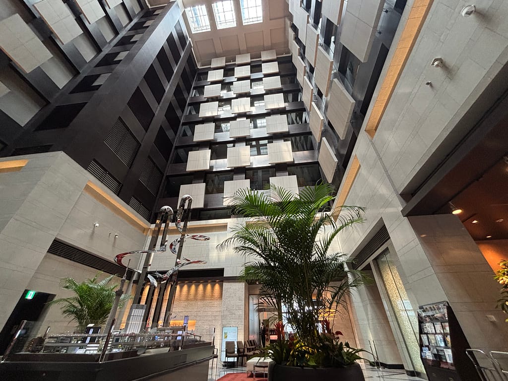 ロビー吹き抜け「ホテルメトロポリタン丸の内の吹き抜けロビー。高い天井と大きな窓から光が差し込み、中央に観葉植物とアートオブジェが飾られている。」