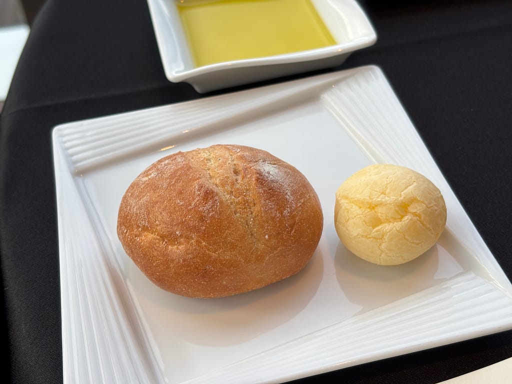 パンとオリーブオイル「小麦パンとチーズ風味の丸パンを白い皿に盛り、オリーブオイルを添えた。」