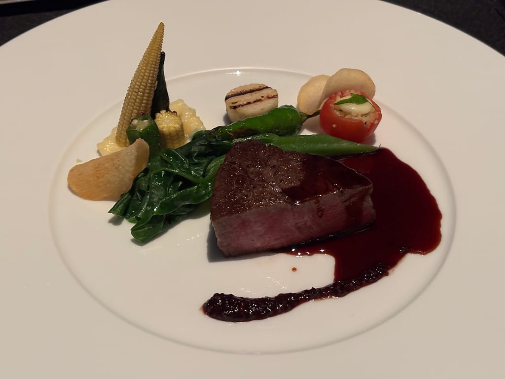 牛フィレ肉のメインディッシュ「牛フィレ肉のステーキと季節野菜の盛り合わせ。赤ワインソースがかかり、彩り豊かな付け合わせが並ぶ。」
