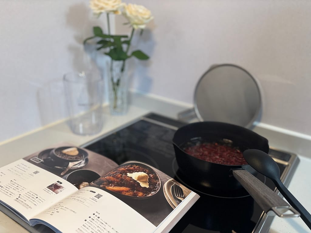 バーミキュラのレシピブックを開き、横で小豆を煮る雪平鍋を並べたキッチンの風景