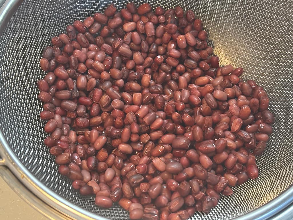 下茹でした小豆を金属製のザルにあけて水気を切っているところ