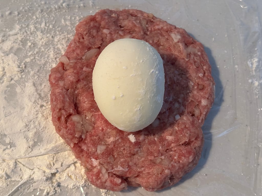 ひき肉で卵を包む工程
「広げたひき肉ダネの上に粉をまぶしたゆで卵をのせ、包む準備をしている」