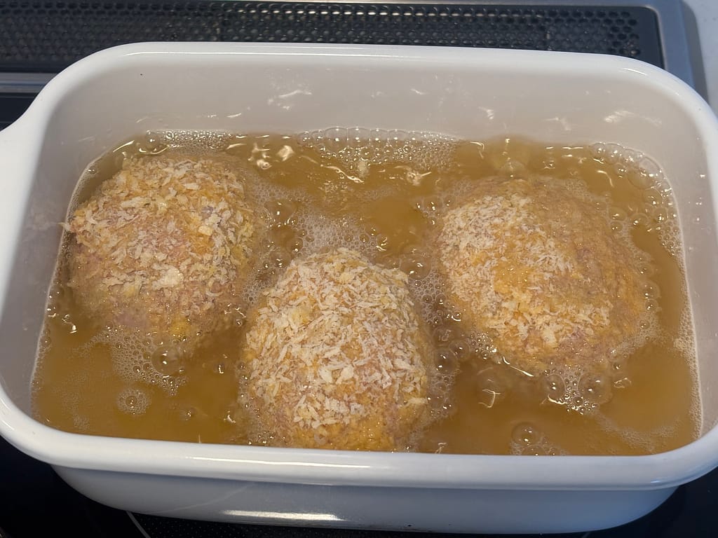 油で揚げる様子
「衣をつけたスコッチエッグを油で揚げている途中。きつね色になり始めた表面」