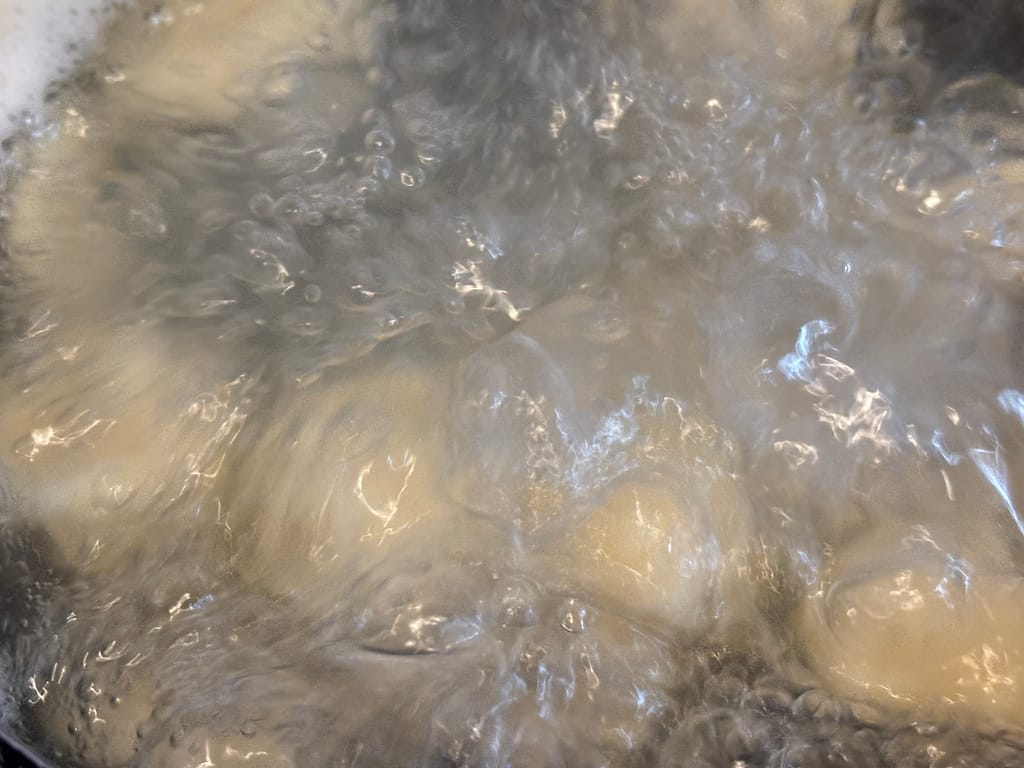 鍋で団子を茹でている様子
沸騰したお湯の中で丸めた団子がぐつぐつ茹でられている場面。表面に泡が立ち、調理中の臨場感が伝わる。